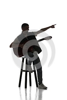 Artistic solo perfumer. Man sitting on chair with guitar isolated over white background. Black and white image.