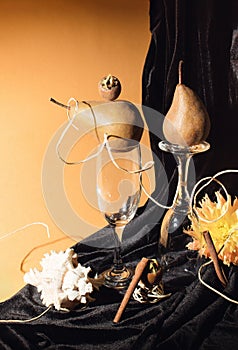 Artistic still life with pears, shell, wine glasses and medlar in combination with orange flower