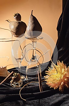 Artistic still life with pears, shell, wine glasses and medlar in combination with orange flower