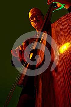 Artistic, talented young bass player performing jazz composition in red-green neon light against gradient studio