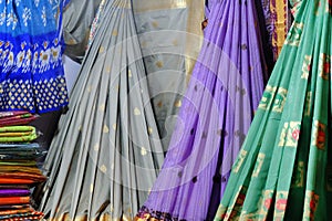 Artistic variety shade tone colors ornaments patterns, closeup view of stacked saris or sarees in display of retail shop
