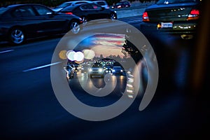 An artistic view of the busy traffic via side mirror at sunset in Los Angeles. Blurred road, headlights and rear lights