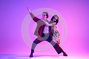 Artistic young man and woman in retro style clothes dancing boogie woogie against purple background in neon light