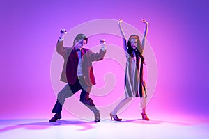 Artistic young man and woman in retro style clothes dancing boogie woogie against purple background in neon light