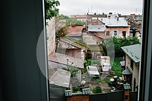 Artwork, noise, grain. View through the window to the old city, retro cars, abandoned houses and overgrown greens