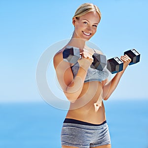 As healthy as can be. Portrait of a smiling young woman lifting weights outside.