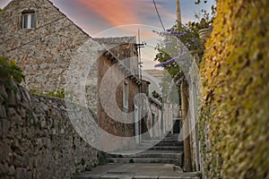 As the sun sets, a pastel sky casts a warm glow over the rustic stone houses of a serene alley in Dubrovnik, Croatia