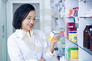 Asain female pharmacist holding and looking medicine packet