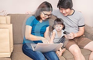 Asain parents and their daughter are doing shopping online using laptop