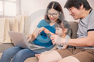 Asain parents and their daughter are doing shopping online using laptop