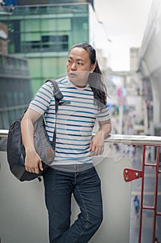 Asain / Thai-Chinese long black hair guy with blue line t-shirt is thinking and holding backpack on his sholder near the sky train photo