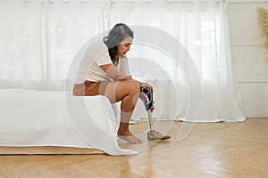 Asain woman with prosthetic leg, seated calmly on a bed