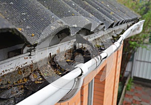 Asbestos house rooftop vinyl rain gutter with fallen leaves and dirt. Gutter cleaning
