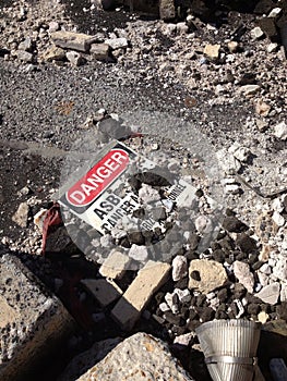 Asbestos warning sign laying among asbestos debris