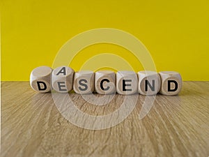 Ascend or descend symbol. Concept words Ascend and Descend on wooden cubes. Beautiful wooden table yellow background.