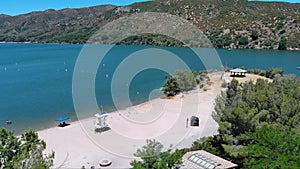 ascending aerial footage of the rippling blue waters of Silverwood Lake with a beach and people swimming in the water