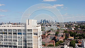 Ascending footage of large building with white facade. Revealing cityscape with skyscrapers in background. London, UK