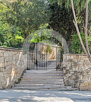 Ascending marble stairs leading to a public park, Stone wall, and fence iron door