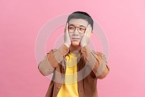 Ashamed man smiling covering his face with hands isolated on a pink background