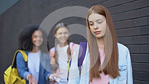 Ashamed red-haired teenager passing by laughing classmates, college bullying