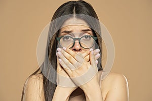 Ashamed woman with hand over mouth on a beige background