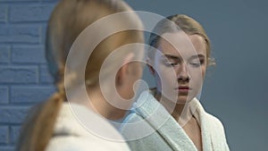 Ashamed young lady in bathrobe looking in mirror, low self-esteem problems