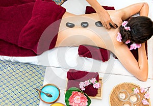 Asia beauty woman lying down on massage bed with traditional hot stones along the spine at Thai spa and wellness center, so relax