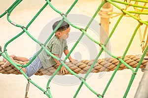 Asia boy enjoying activity in a climbing adventure park on a summer day. Boy climbing ropes