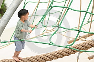 Asia boy enjoying activity in a climbing adventure park on a summer day. Boy climbing ropes