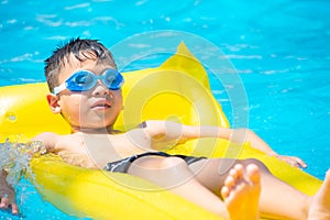 Asia boy wearing swimming goggles on yellow protrude in a swimming pool photo