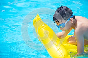 Asia boy wearing swimming goggles on yellow protrude in a swimming pool photo