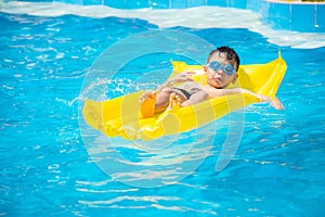 Asia boy wearing swimming goggles on yellow protrude in a swimming pool photo