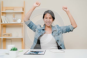 Asia business woman success celebration keeping arms raised at home office. Young asian woman working writing notebook document