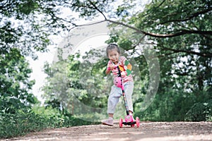 Asia children learn to ride scooters in a park on a summer day. Preschooler girl riding a roller. Kids play outdoors with scooters
