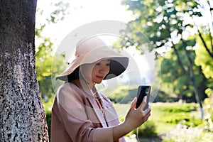 Asia Chinese beautiful woman wear earphones listen to music enjoy cozy afternoon in Spring outdoor park forest peaceful life