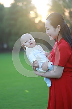 Asia Chinese happy mom hug hold kiss new-born chubby baby park forest outdoor in summer love peace smile bathed in sun portrait