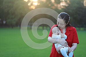 Asia Chinese happy mom hug hold kiss new-born chubby baby park forest outdoor in summer love peace smile bathed in sun portrait