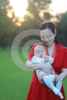 Asia Chinese happy mom hug hold kiss new-born chubby baby park forest outdoor in summer love peace smile bathed in sun portrait