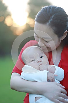 Asia Chinese happy mom hug hold kiss new-born chubby baby park forest outdoor in summer love peace smile bathed in sun portrait