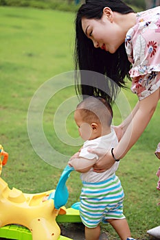 Asia Chinese woman held help little toddler baby boy son learn to walk maternal love family on lawn outdoor in summer walker