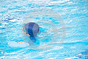 Asia cute boy wearing swimming suit and goggles used foam to practice swimming in swimming pool. Healthy kid enjoying active