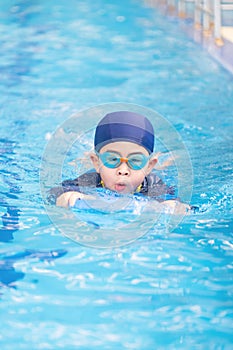 Asia cute boy wearing swimming suit and goggles used foam to practice swimming in swimming pool. Healthy kid enjoying active