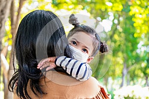 Asia cute girl daughter hugging mom in the garden on blurred background. Kid wearing hygiene medical face mask to protect