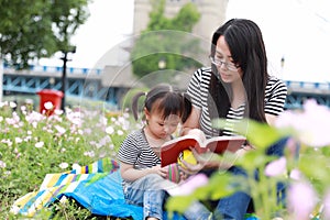 Asia cute laugh lovely adorable girl read book with mother enjoy free day with mom tell story outdoor in summer park happy smile