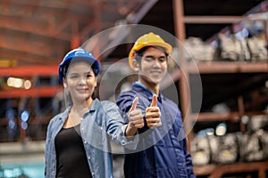 Asia engineer woman and man worker wear a safety helmet and thumb up, look at the camera. Standing in the automotive spare parts