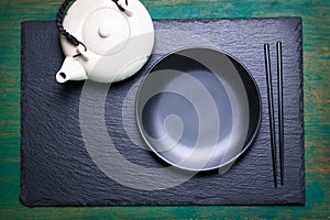 Asia food composition with chinese chopsticks, teapot and empty plate on a dark stone background