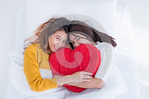 Asia lesbian LGBT Couple lay on bed and hug rainbow color pillow heart shape with happiness moment together,love win concept