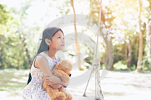 Asia little girl with doll bear sitting on a swing .