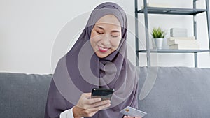 Asia muslim lady use smart phone, credit card buy and purchase e-commerce internet in living room at house.