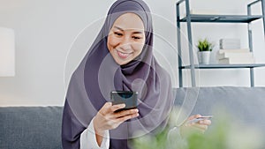 Asia muslim lady use smart phone, credit card buy and purchase e-commerce internet in living room at house. Stay at home, online